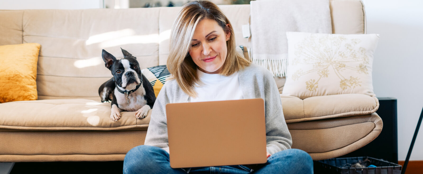 Woman using a laptop with her dog sitting behind her